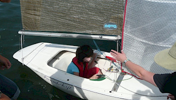 Ein Kind sitzt in einem kleinen einsitzigen Segelboot.